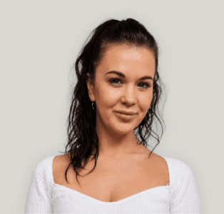 Shelley Portrait of a woman with dark hair tied back, wearing a white knit top, looking at the camera.